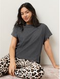 Vrouw met donkergrijs T-shirt en luipaardprint broek zit op de grond.