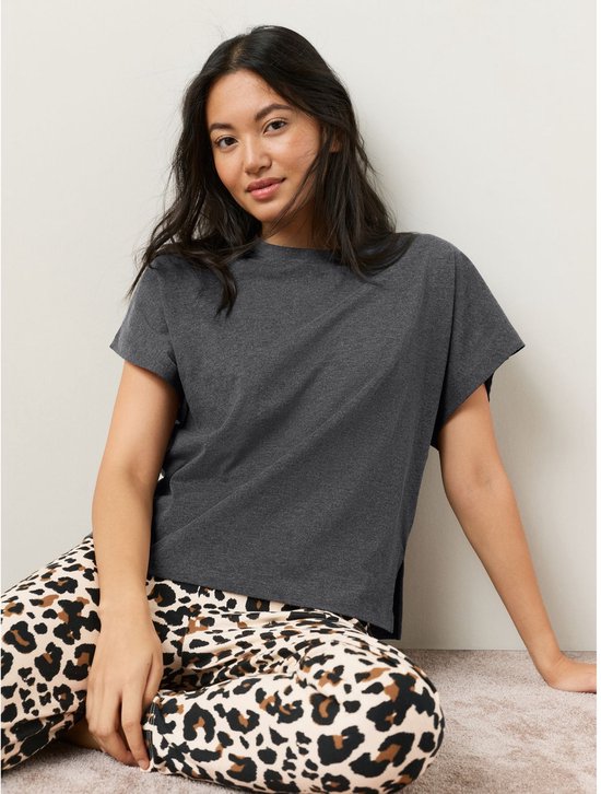 Vrouw met donkergrijs T-shirt en luipaardprint broek zit op de grond.