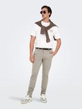Man in een beige chino, wit T-shirt met print, bruine trui over de schouders, zonnebril en sneakers.