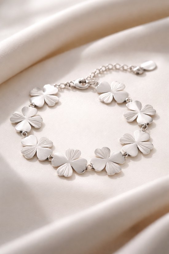 Bracelet argenté avec maillons trèfle à quatre feuilles sur un tissu doux de couleur crème.