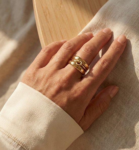 Main féminine portant des bagues empilables Lundholm dorées de la série Helena, avec un nœud infinity.