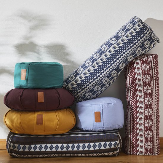 Bolsters de yoga empilés dans différentes couleurs et motifs : vert, bordeaux, jaune, bleu clair et deux avec des motifs brodés.