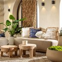 Loungebank met beige kussen, sierkussens met visjes en schelp, plus planten en houten tafels.