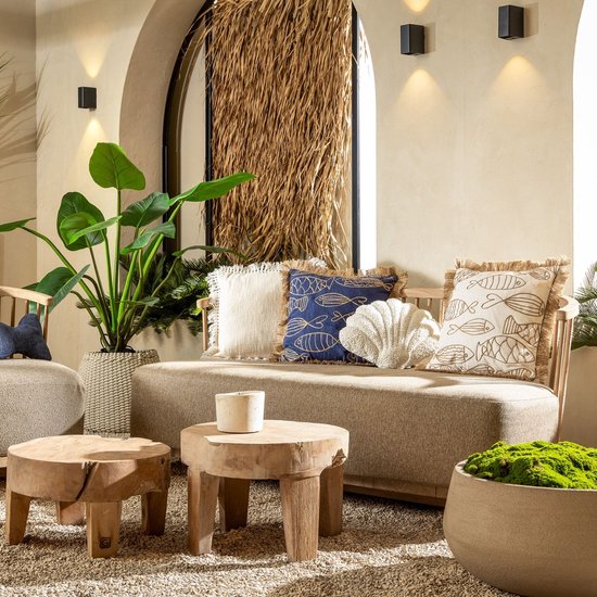 Loungebank met beige kussen, sierkussens met visjes en schelp, plus planten en houten tafels.