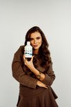 Een vrouw met lang bruin haar houdt een fles 'CAL-MAG 33 SHOTS' vast.