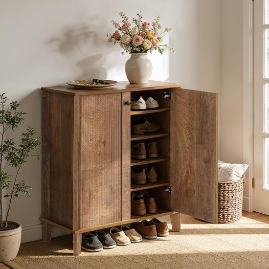 Meuble à chaussures en bois avec portes ouvertes, rempli de chaussures. Vase de fleurs et plante à côté.