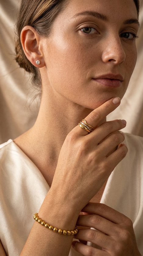 Model draagt gouden kralenarmband van 4 mm, gelaagde ringen en oorbellen.