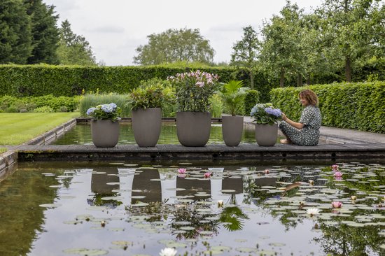 Vijf taupe bloempotten met ribbelpatroon, gevuld met planten en bloemen, staan op een houten vlonder aan een vijver.