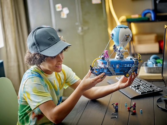 Un garçon tient le LEGO Fortnite Battle Bus avec un ballon, avec des figurines dessus.