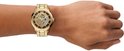 Pols met een goudkleurig Fossil skeleton horloge met metalen band, op de achtergrond is een deel van de hand te zien.