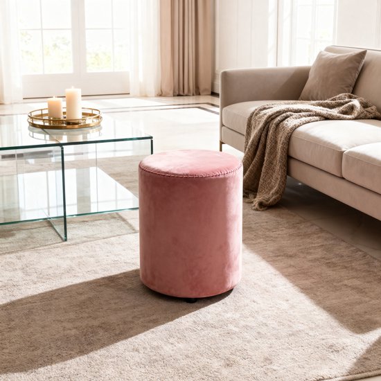 Roze fluwelen poef in een woonkamer naast een bank.