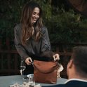 Een lachende vrouw in een grijze blouse met een cognac leren schoudertas van The Chesterfield Brand.