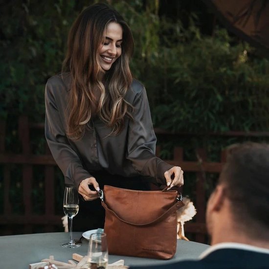 Een lachende vrouw in een grijze blouse met een cognac leren schoudertas van The Chesterfield Brand.