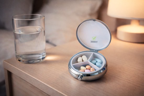 Zilverkleurig open pillendoosje met drie vakken, gevuld met gekleurde pillen, op een nachtkastje naast een glas water.