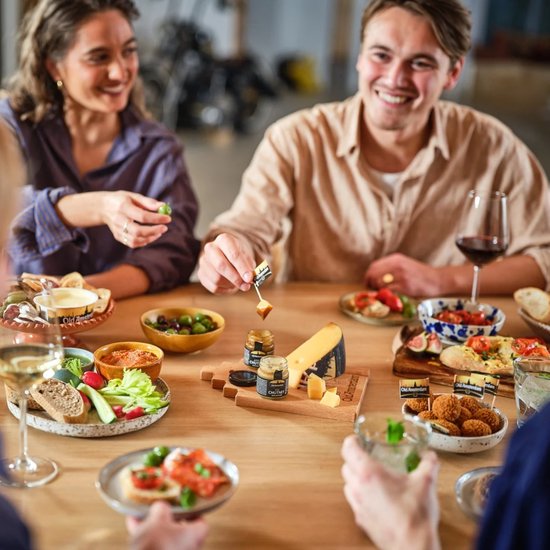 Mensen genieten van een kaasplank met Old Amsterdam kaas, chutney, olijven en brood.