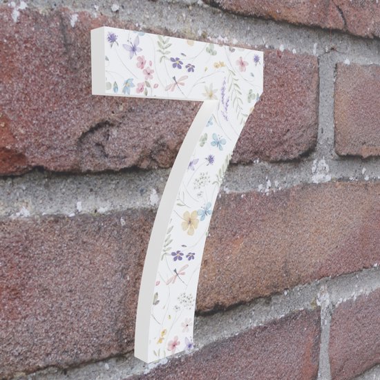 Huisnummer 7 met een patroon van lila, roze, gele en blauwe bloemen, takjes en libellen op een witte achtergrond, vastgeplakt op een bakstenen muur.