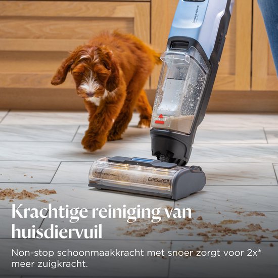 Een bruine hond rent weg van een stofzuiger met ledverlichting op een lichte vloer bedekt met dierenharen en vuil.
