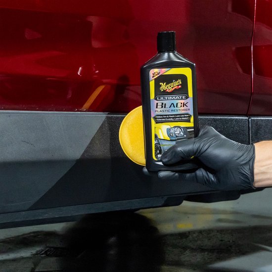 Hand in zwarte handschoen brengt Meguiar's Ultimate Black aan op zwarte kunststof auto-onderdeel.