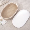 Ovalen babywieg van gevlochten touw met witte matras ernaast. De binnenkant is beige en de buitenrand is wit.