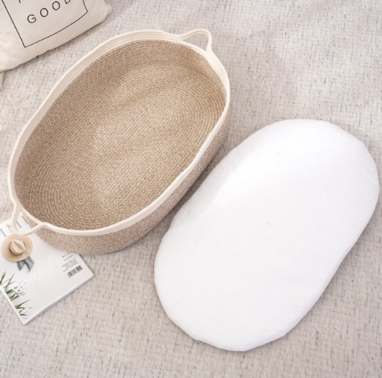 Ovalen babywieg van gevlochten touw met witte matras ernaast. De binnenkant is beige en de buitenrand is wit.