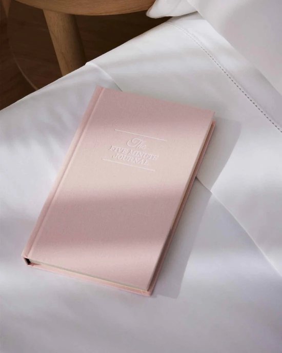 Blushroze 'The Five Minute Journal' liggend op wit beddengoed.