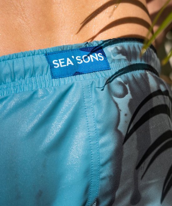 Blauwe zwembroek met een label waarop 'SEA'S SONS' staat. De zwembroek heeft een lichtblauwe tailleband en een grijze, palmblad-achtige print.