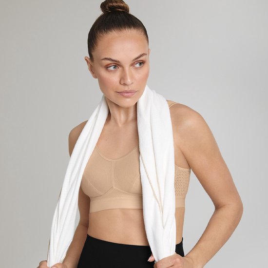 Vrouw met staartje, draagt een beige sportbeha, met een witte handdoek om haar nek.
