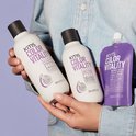 Handen houden KMS COLOR VITALITY shampoo, conditioner en gloss treatment in paarse en witte verpakkingen.