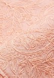 Gedetailleerde close-up van perzikkleurige kanten stof met geborduurd bloemen- en paisley-patroon.