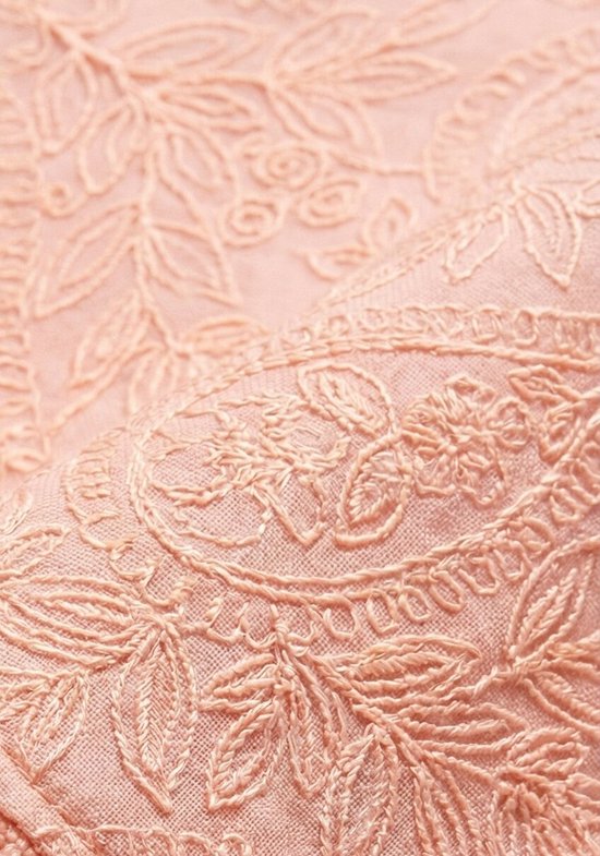 Gedetailleerde close-up van perzikkleurige kanten stof met geborduurd bloemen- en paisley-patroon.
