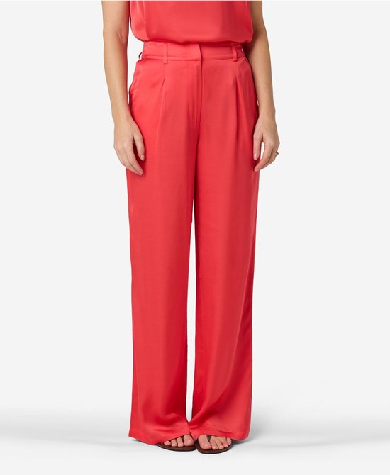 Vrouw in een koraalrode satijnen broek met wijde pijpen, gulpplooien en een riem.