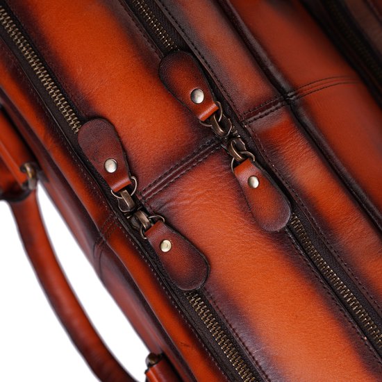 Detail van de metalen ritsen en leren lipjes op een bruine leren tas.