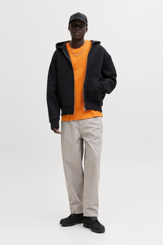 Man draagt oranje wafel t-shirt met zwarte hoodie, beige broek en zwarte pet.