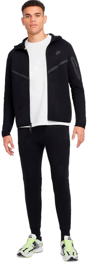 Man draagt een zwarte Nike Tech Fleece hoodie met rits en een witte T-shirt.