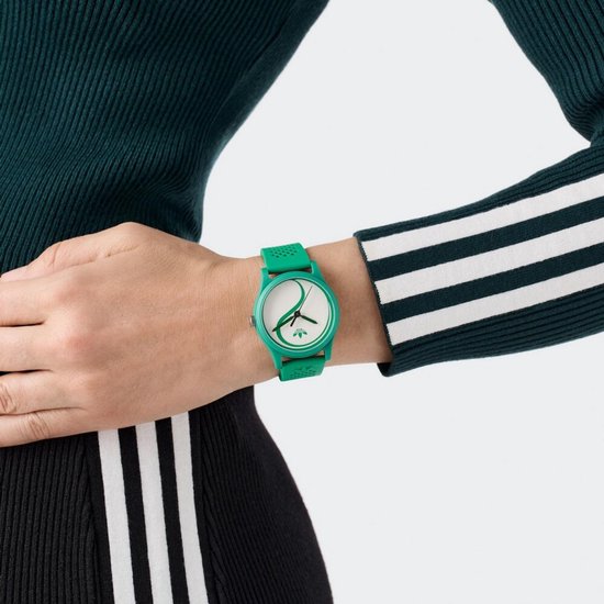 Groen Adidas horloge met witte wijzerplaat met yin-yang-achtig groen patroon, gedragen om een pols.