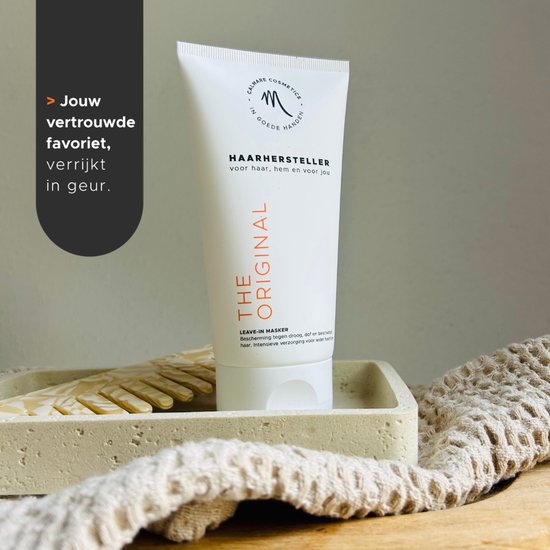 Witte tube met de tekst 'THE ORIGINAL HAARHERSTELLER' en een logo. Naast de tube liggen een beige handdoek en twee beige handschoenen.