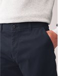 Detailopname van een marineblauwe chinobroek met knoopsluiting en hand in de zak.