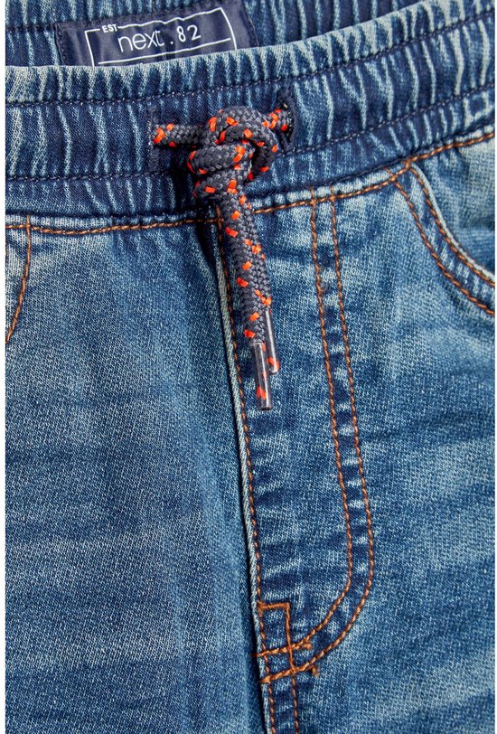 Detail van de tailleband en het trekkoord met oranje accenten van een jongens jeans.