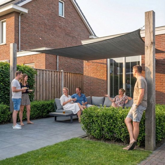 Groep mensen ontspant onder een groot zwart schaduwdoek in een tuin.