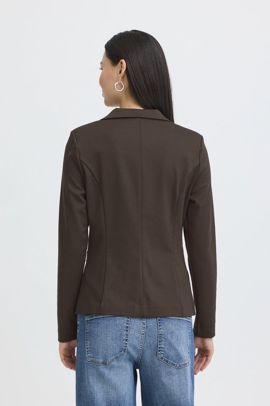 Vrouw met lange donkere haren, de achterkant van een bruine blazer en spijkerbroek.