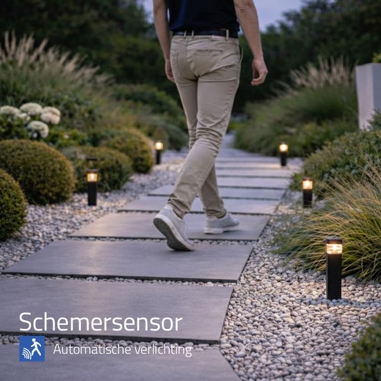 Man loopt over een tuinpad met vierkante, zwarte staande lampen met warm wit licht en schemersensor.