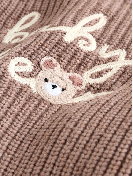 Detail van het borduurwerk met een teddybeer en de tekst "baby bear" op een bruine gebreide trui.