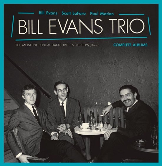Bill Evans Trio, het meest invloedrijke pianotrio in moderne jazz, compleet. Drie mannen in pak zitten aan een tafel in een donkere kamer.