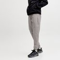 Man met grijze joggingbroek, zwarte jas en zwarte sneakers, staand op witte achtergrond.