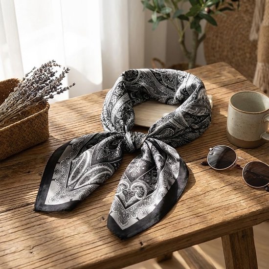 Geknoopte zwart-witte paisley sjaal op een houten tafel met een kopje en zonnebril.