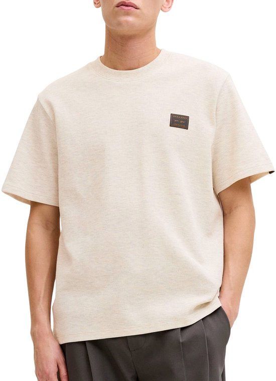 Homme portant un T-shirt crème à texture gaufrée, col rond et un écusson logo marron sur la poitrine gauche.