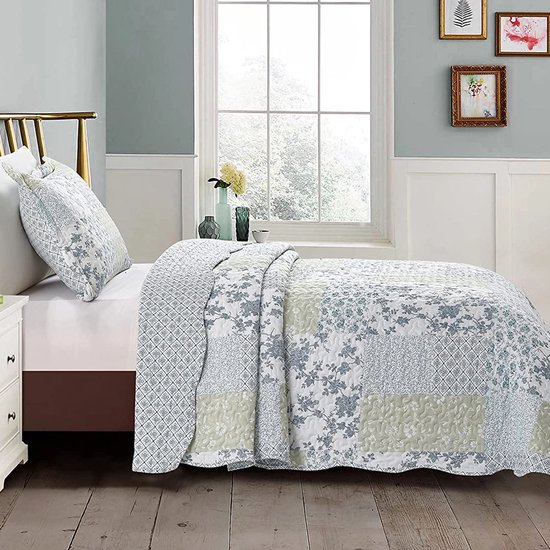 Bed met patchwork quilt in blauw en groen, met bloemenprints en ruitpatronen. Sierkussensloop met dezelfde patronen.