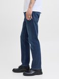 Jonge man met tatoeages, zittend, met ringen, in een witte T-shirt en donkere jeans.