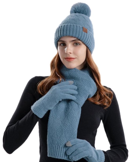 Model draagt een blauwe gebreide set met muts met pompon, sjaal en handschoenen met textuurpatroon.