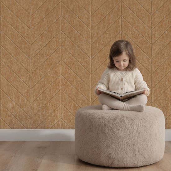 Une petite fille lit un livre sur un pouf devant un mur brun beige à motif chevrons.